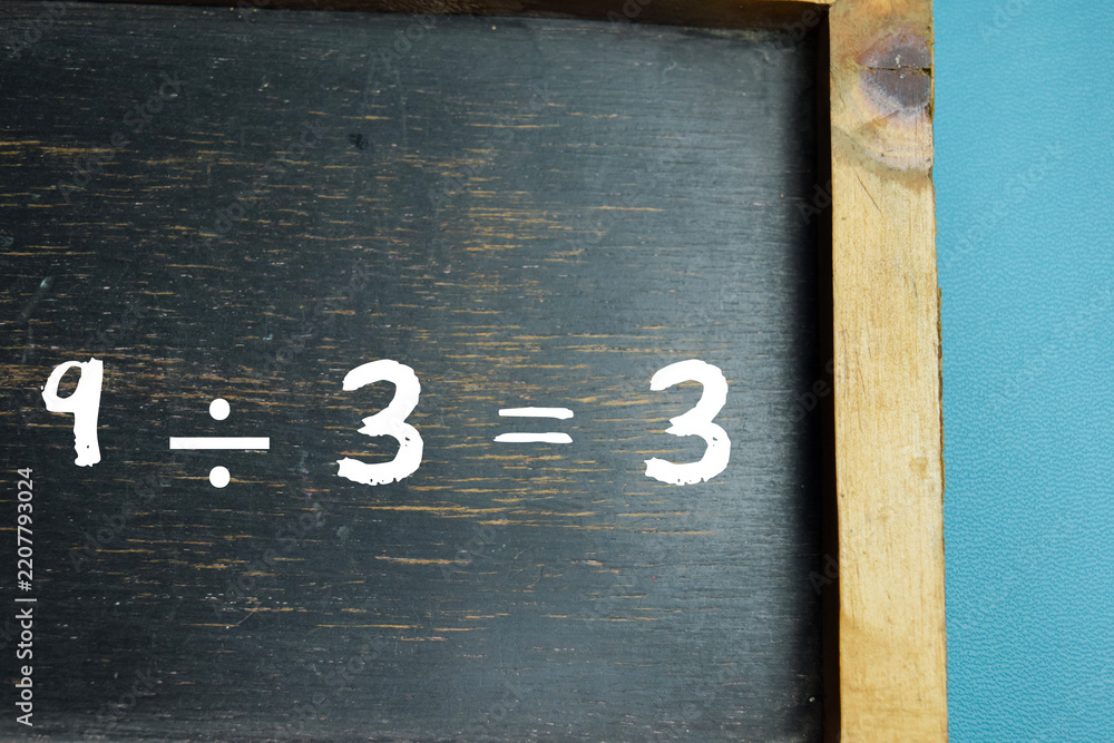 Obraz premium Chalkboard with phrase 9 ÷ 3 = 3 division equation on wooden desk. For school education and learning