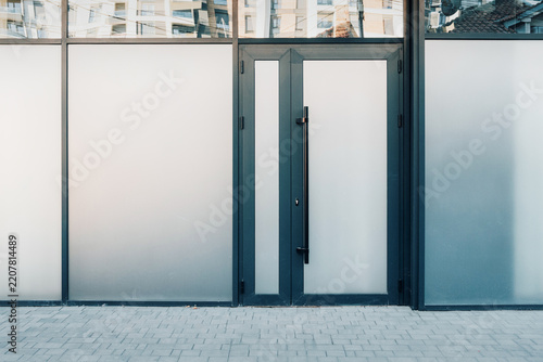 Modern building entrance featuring a dark framed glass door and surrounding frosted windows, reflecting urban architecture
