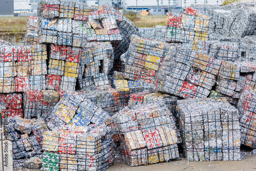 Compressed aluminum cans form dense metal bales stacked at recycling facility. Industrial waste processing scene shows scrap recovery, sorting, reuse, sustainability, circular economy and resources