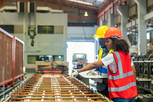 Two factory workers wearing safety helmets inspecting machinery and discussing work inside an industrial plant.
