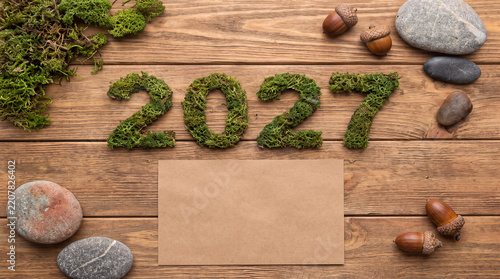 A rustic wooden background nicely frames the year 2027 accompanied by carefully scattered natural stones and pinecones.