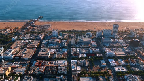 Santa Monica waterfront blocks and pier from above. An elevated view looks across rooftops toward the sandy shore and sunlit ocean.
