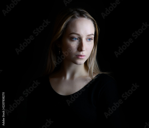 Elegant young woman in black clothing portrayed against a dark background