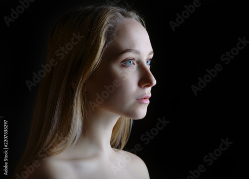 Elegant blonde woman in profile illuminated against a dramatic black background