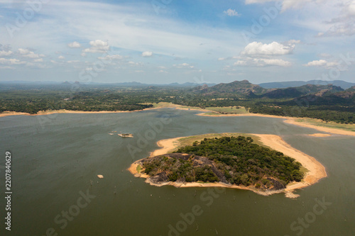 Aerial view of lake with an island in the middle of a tropical forest on the background of mountains. Kandalama Reservoir in Sri Lanka.
