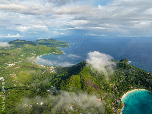 Turquoise waters of a bay surrounded by lush green hills and a scattering of fluffy clouds in the sky. Seychelles, Mahe.