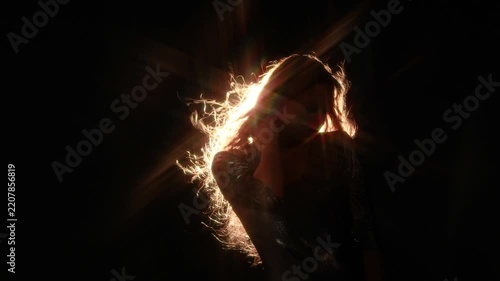 Elegant woman in a shiny silver dress with flying hair in the spotlight. Star shaped flare and warm rim light on black for club and evening event promo.