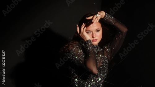 Woman in a crystal gown reaching to the light with open arms. A narrow beam and sparkling stones against darkness give a feeling of release and power.
