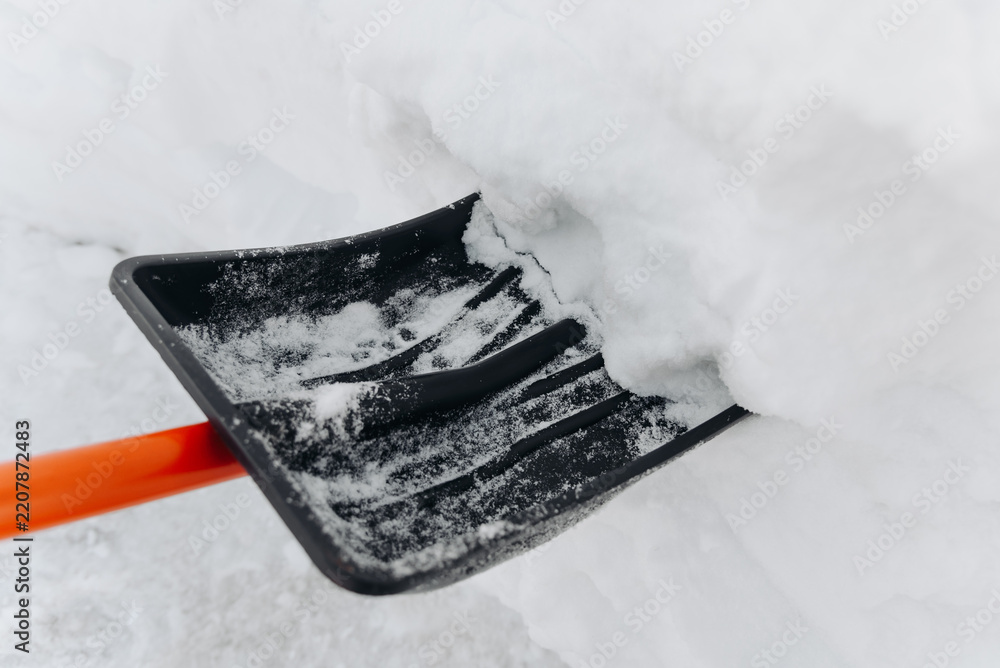 Fototapeta premium snow shovel in snow, cleaning territory of snow, courtyard, path, garden, black and orange shovel, snowfall, atmospheric precipitation, bad weather conditions