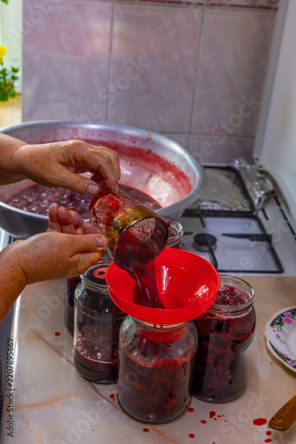 Hands Pouring Homemade Strawberry Jam into Glass Jars