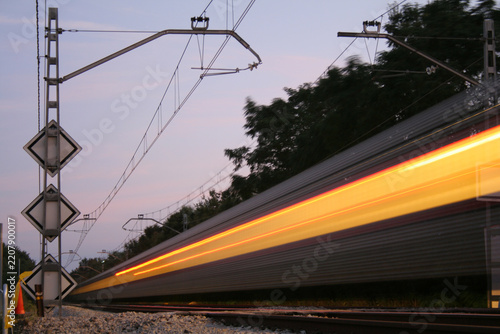 Obraz na plátně High-speed train passing by with motion blur effect and a glowing light trail on railway tracks at dusk