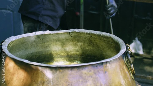 Chef lifts large pieces of meat with metal hook from boiling broth in ancient kazan for Uzbek plov