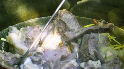 Chef in gloves stirs boiled meat for plov in a large cauldron