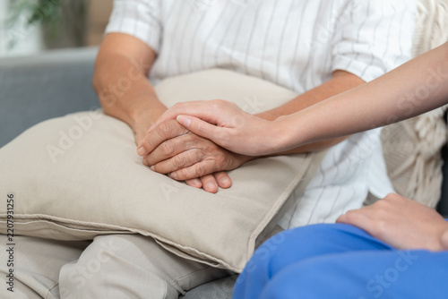 Young hand rests on wrinkled hands of senior woman on beige cushion, close-up image of trust, care and support between caregiver and elderly patient.