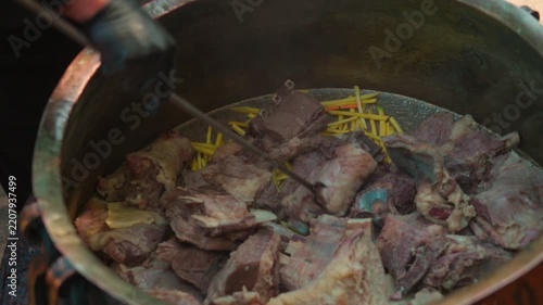 Chef in Black Gloves Adding Large Meat Chunks to Old Metal Kazan for Pilaf
