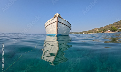 White boat floats calmly on clear blue aegean sea in Greece