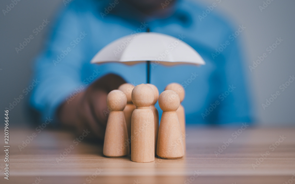 Obraz premium Insurance protection, security, safety, healthcare concept, hand holding an umbrella over group of wooden people figures.