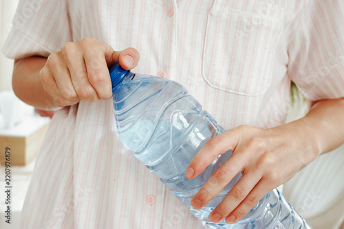 Fotografie Close-up of hands removing the blue cap from a large transparent plastic drinking water bottle
