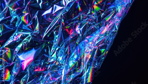 A close-up shot of crumpled holographic plastic material reflecting a spectrum of rainbow colors against a dark background.