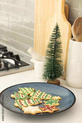 Blue plate is holding iced christmas tree and snowflake cookies on counter near stove
