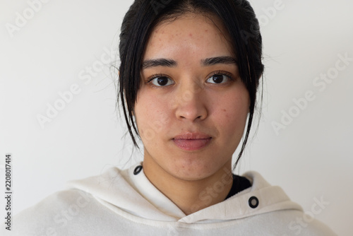 Woman wearing light hoodie with black grommets and dark top looking at camera in studio