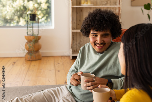 African American couple sitting on low sofa holding ribbed mugs, wearing sage-top mustard-sweater