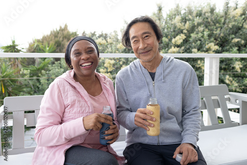 Diverse couple with senior Asian man and woman sitting on balcony holding clear bottles