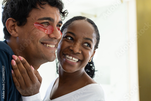 African couple smiling together at home, man wearing red hydrogel patches, woman showing pink nails