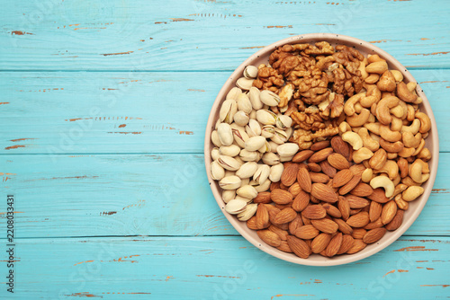 Mix of various nuts on plate on blue background. Pistachios, cashews, walnuts, hazelnuts, peanuts. Space for text