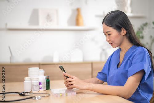 Asian female nurse checking pill organizer and medicine bottles with smartphone for medication safety, Medical professional preparing daily dosages, Patient safety and digital healthcare tech concept