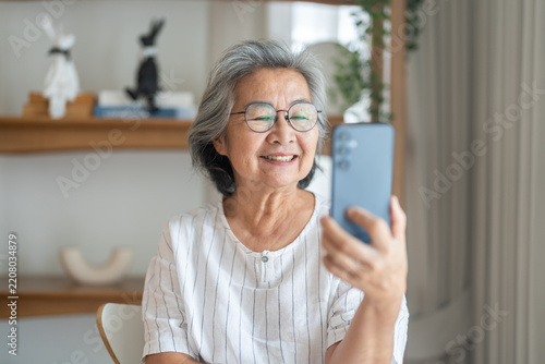 Asian elderly woman using smartphone for social connection at home, Smiling senior female having digital communication on mobile phone, Modern technology and happy healthy aging lifestyle concept