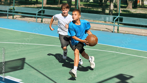 Fotografie Energetic adolescent player runs with the basketball while a rival gives chase on a sunny court