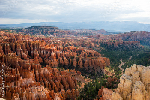 View of Bryce Canyon National Park with its iconic orange hoodoos and pine trees under a cloudy sky in Utah, United States.
