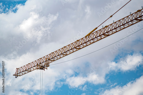 Yellow construction crane jib extending across a cloudy blue sky. This industrial image is perfect for real estate development, construction management, and urban growth marketing materials.