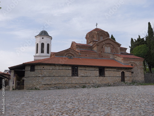 View of the Church of the Virgin Mary Peribleptos with its distinctive red-tiled roof, stone walls, and bell tower, set against a cloudy sky in Ohrid, Municipality of Ohrid, North Macedonia.