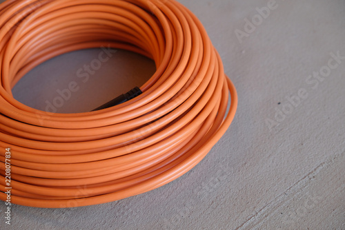 Close-up: a coil of orange cable and laid-out loops on a concrete screed, secured with mounting tape. Construction work.