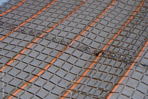 Installation of electric underfloor heating: orange heating cable and basalt reinforcement mesh on a concrete floor.