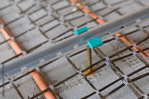 Fastening a screed rail to the floor using a clip and a self-tapping screw. Close-up of the screed installation.