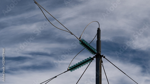 View of high voltage power lines with glass insulators on a metal pylon against a cloudy sky in Iceland.