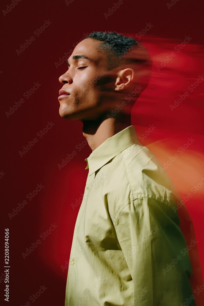 Fototapeta premium Side profile of a man with motion blur on a bold red background wearing a lime shirt in a minimalist expressive portrait