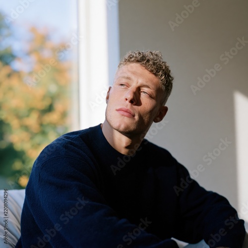 Young man in navy sweater moody window portrait with warm sidelight and reflective mood for personal profile and social media header