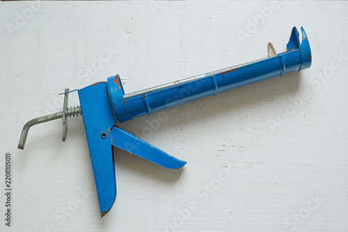 An old, blue caulking gun rests on a weathered white wooden surface.