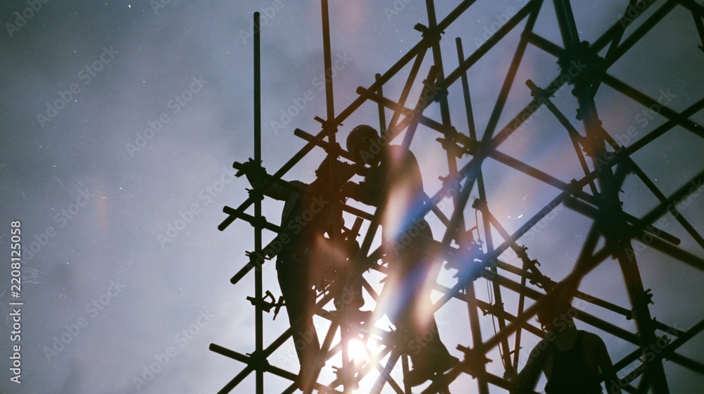 Obraz premium Silhouette of Construction Workers on Metal Scaffolding at Sunset