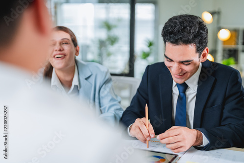 diverse team collaborates during a business meeting, smiling and engaged around a laptop displaying data charts. This candid office moment captures teamwork, professionalism, and positive workplace co