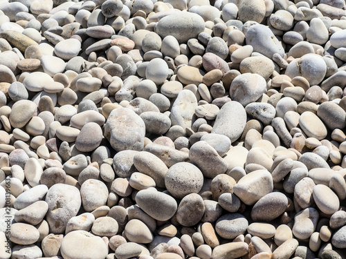Fotografie Smooth rounded beach pebbles in sunlight, full frame natural stone background