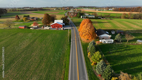 Aerial view of a rural road cutting through farmland with a red barn, autumn foliage, and residential properties in Rapho, Pennsylvania, United States.