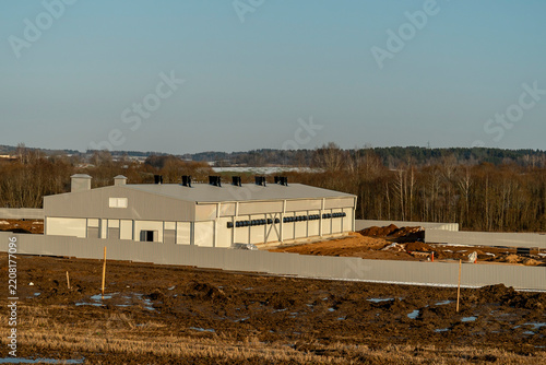 A construction project is underway in a rural setting, featuring expansive open fields and beautiful trees in the backdrop