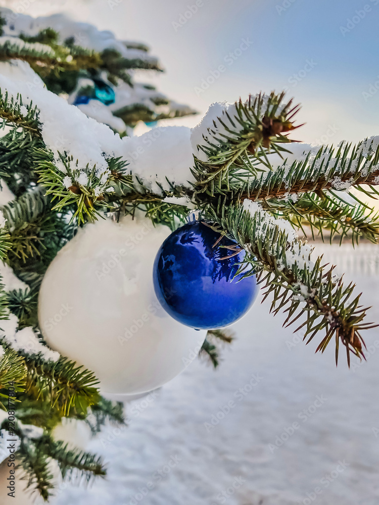 Obraz premium A natural Christmas tree stands decorated with ornaments and snow. It is winter, and the scene shows a festive atmosphere during the New Year celebration