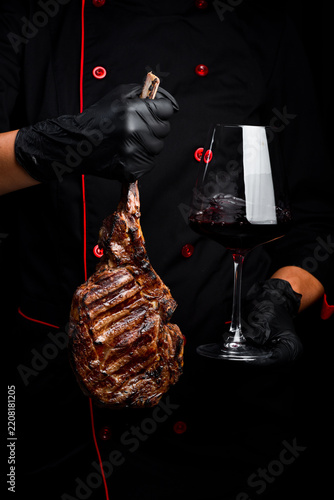 Tomahawk steak and a glass of wine in the hands of the chef. Close-up. On a black background.