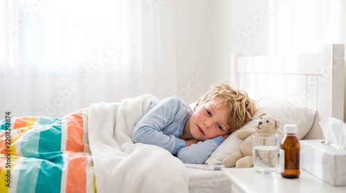 Sick child in bed looking unwell and resting under a colorful blanket  
